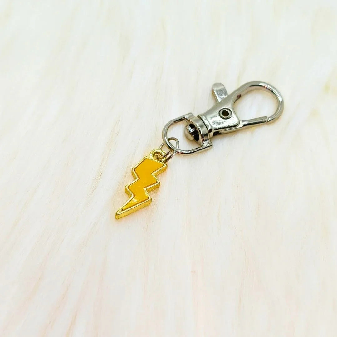 Yellow lightning bolt phone charm with metal clasp on soft cream background