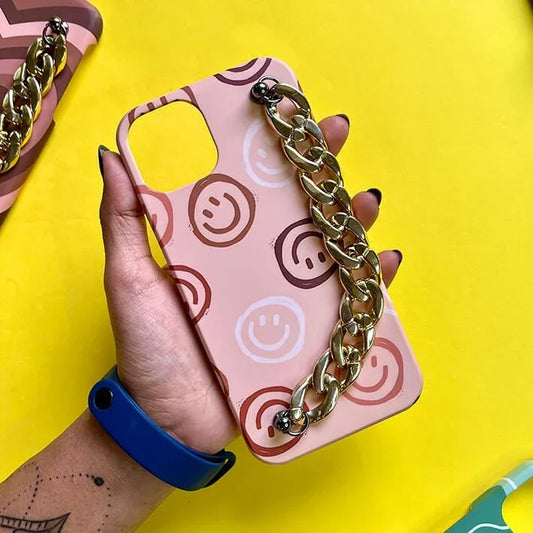 Pink phone case with smiley face design and gold chain strap, held in hand on yellow background